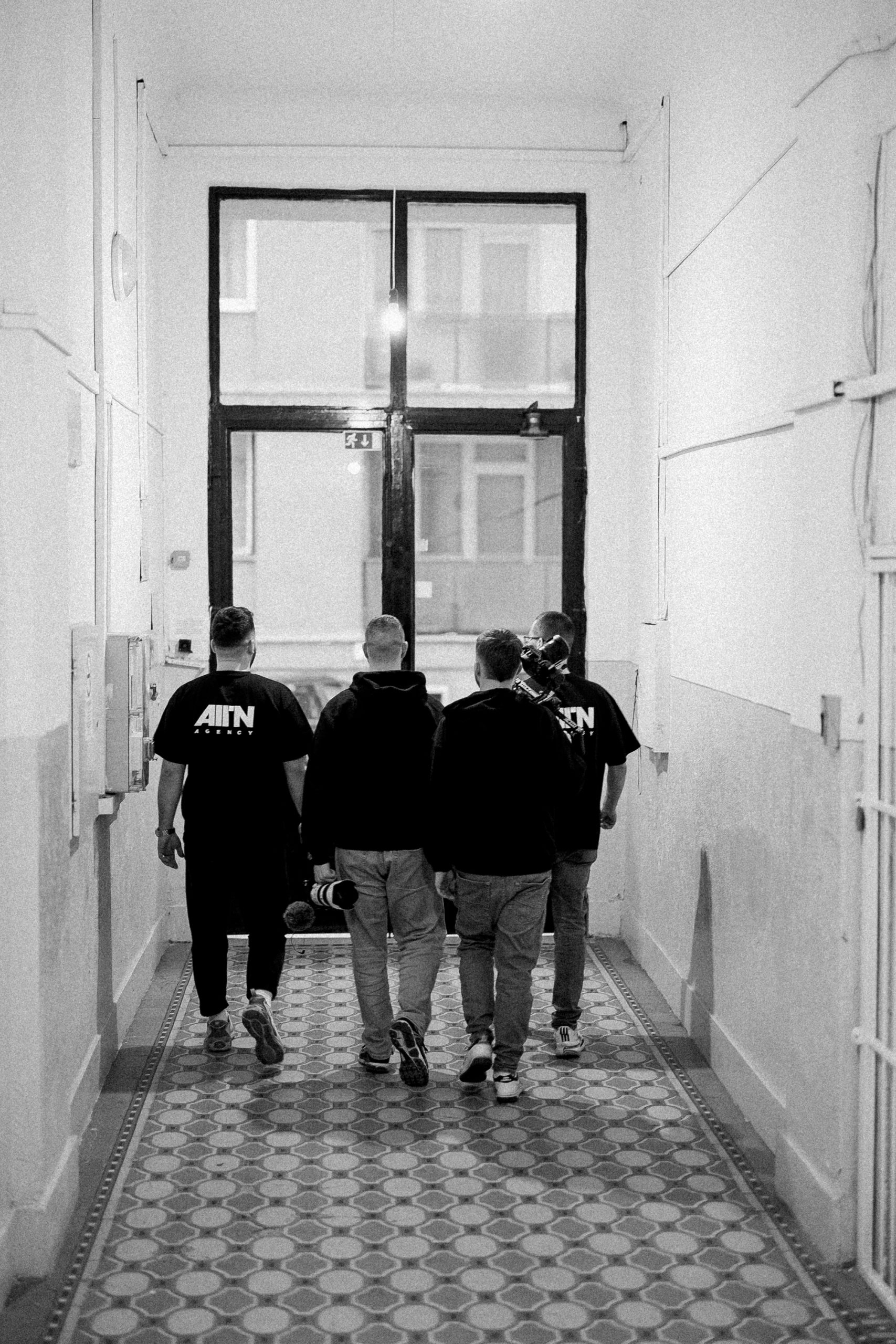 Négy ALLIN Agency csapattag hátulról egy lépcsőház folyosóján, forgatás után