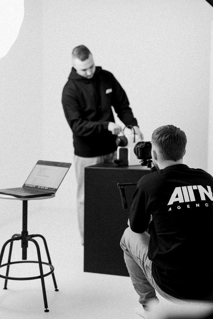 Stúdió termékfotózás: ALLIN Agency csapattag kamerával, háttérben a beállítást végző kollégája